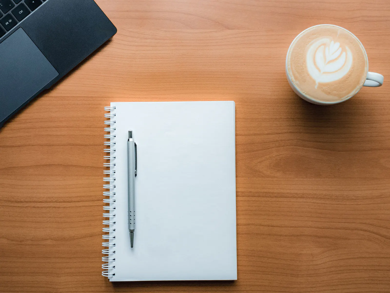 Blank spiral notebook, pen and cup of coffee on a wooden table