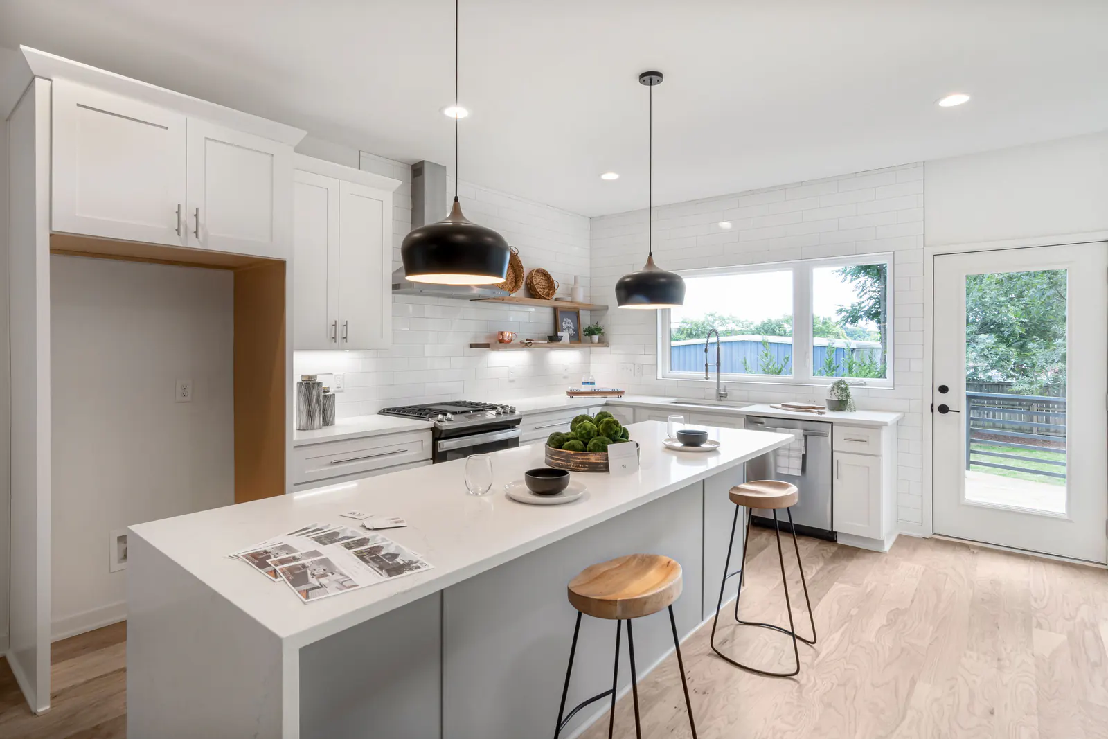 Bright white kitchen with island, wooden stools and black pendant lights