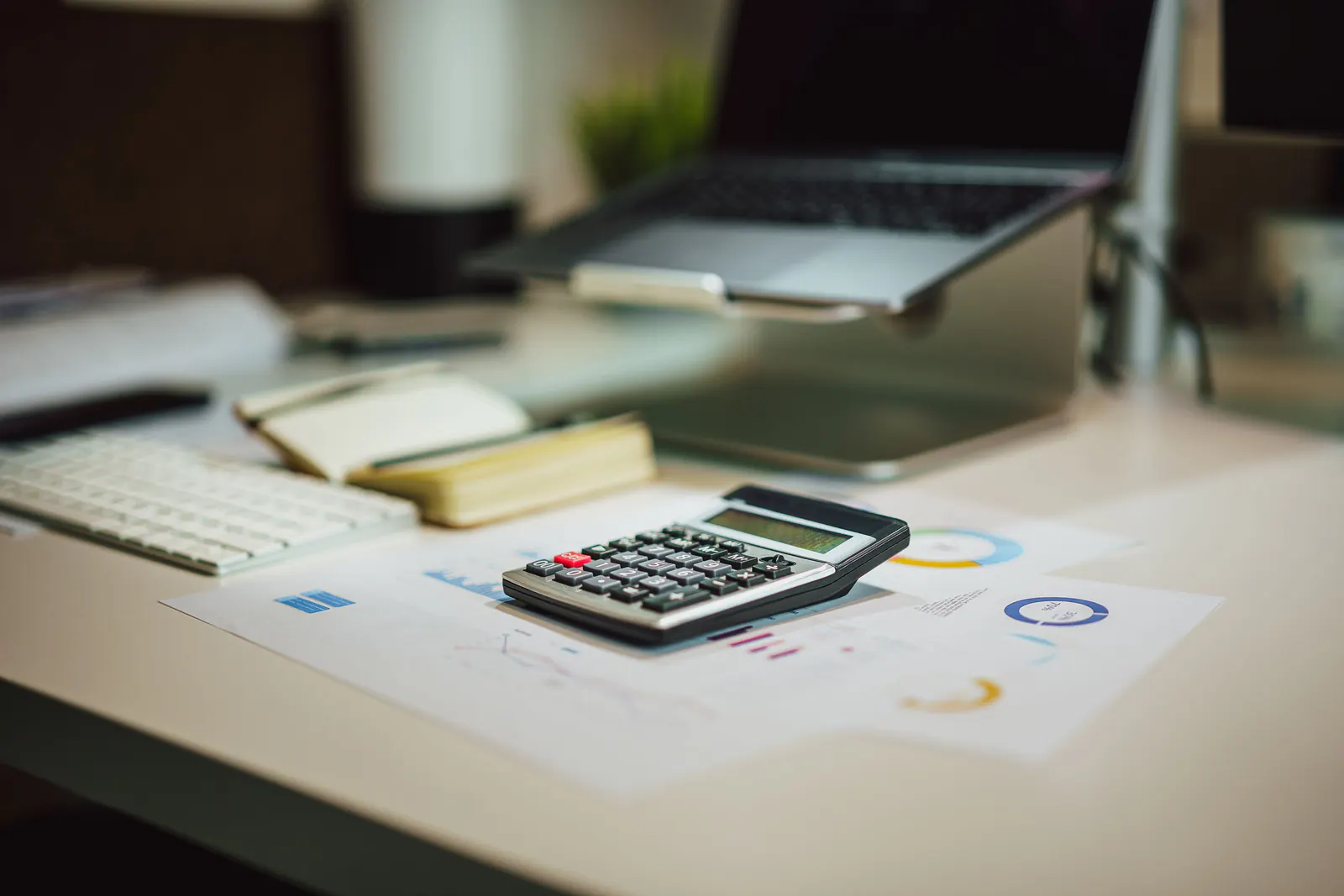 Calculator and printed charts on a desk beside a laptop and keyboard