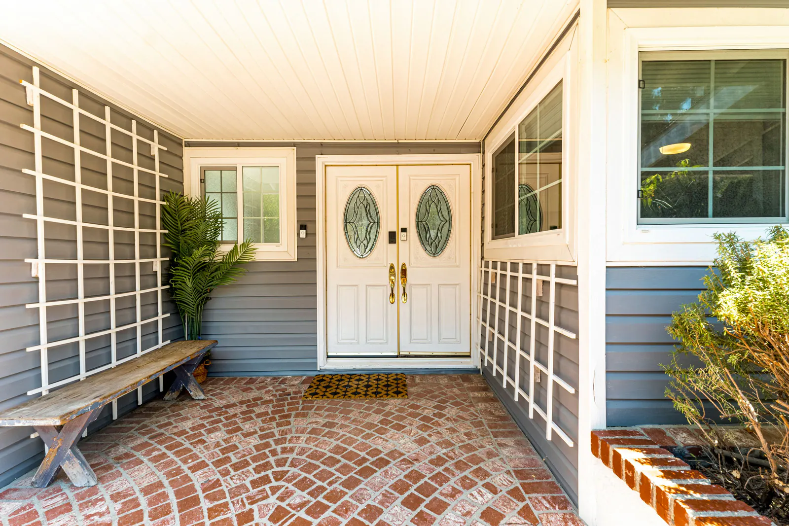 Covered front entry with white double doors, brick floor, bench and plant