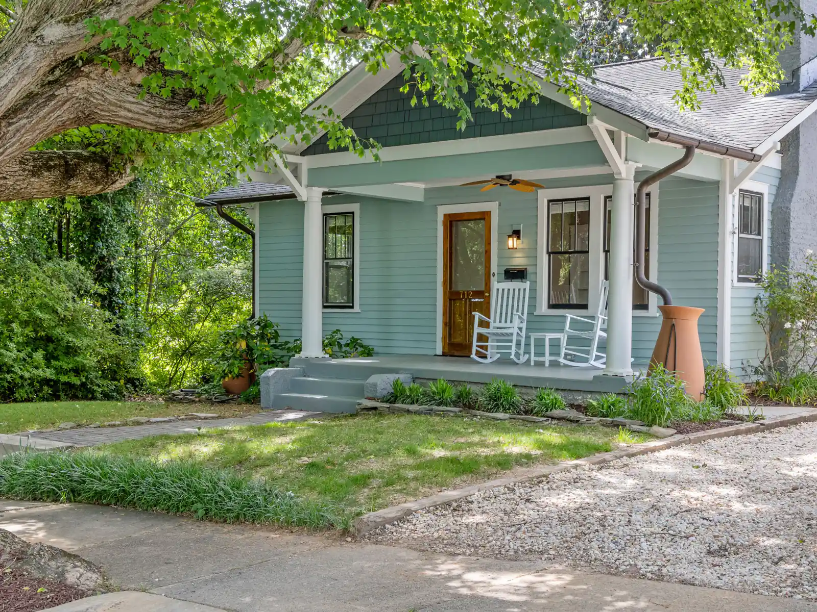 Pale green craftsman bungalow with rocking chairs on a shaded front porch