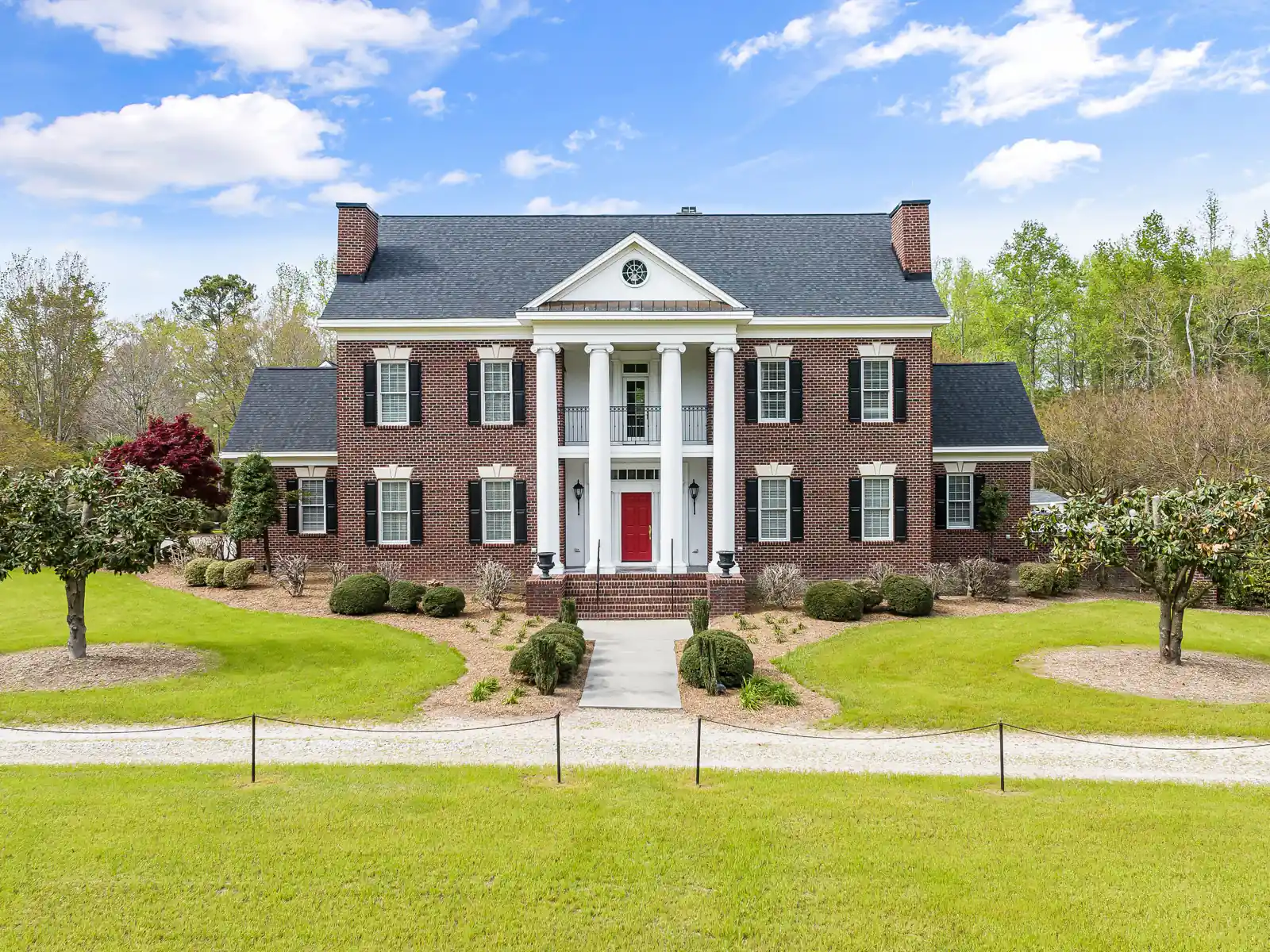 Large red brick home with white columns behind a wide green lawn