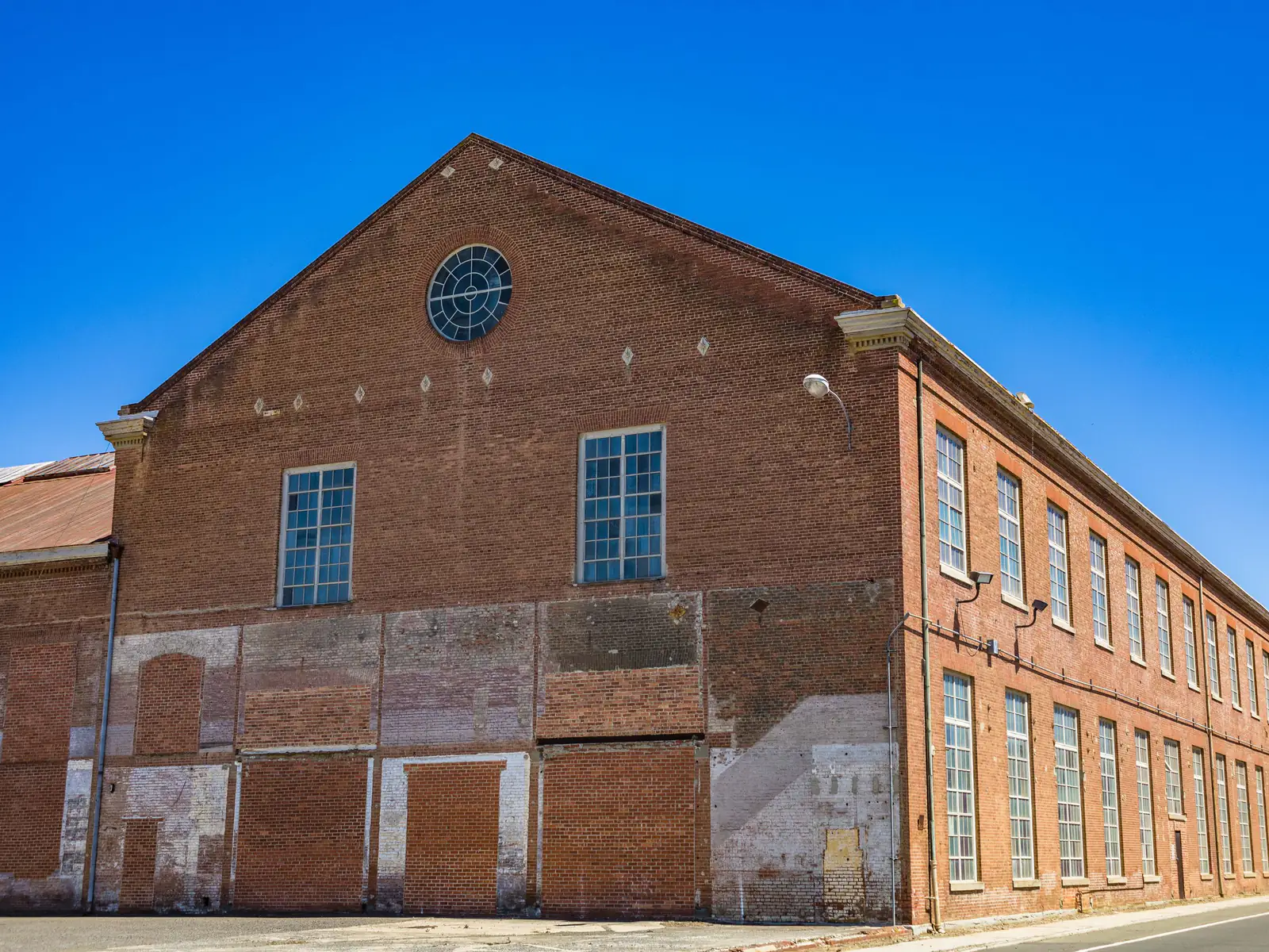 Long red brick mill building with tall windows under a blue sky