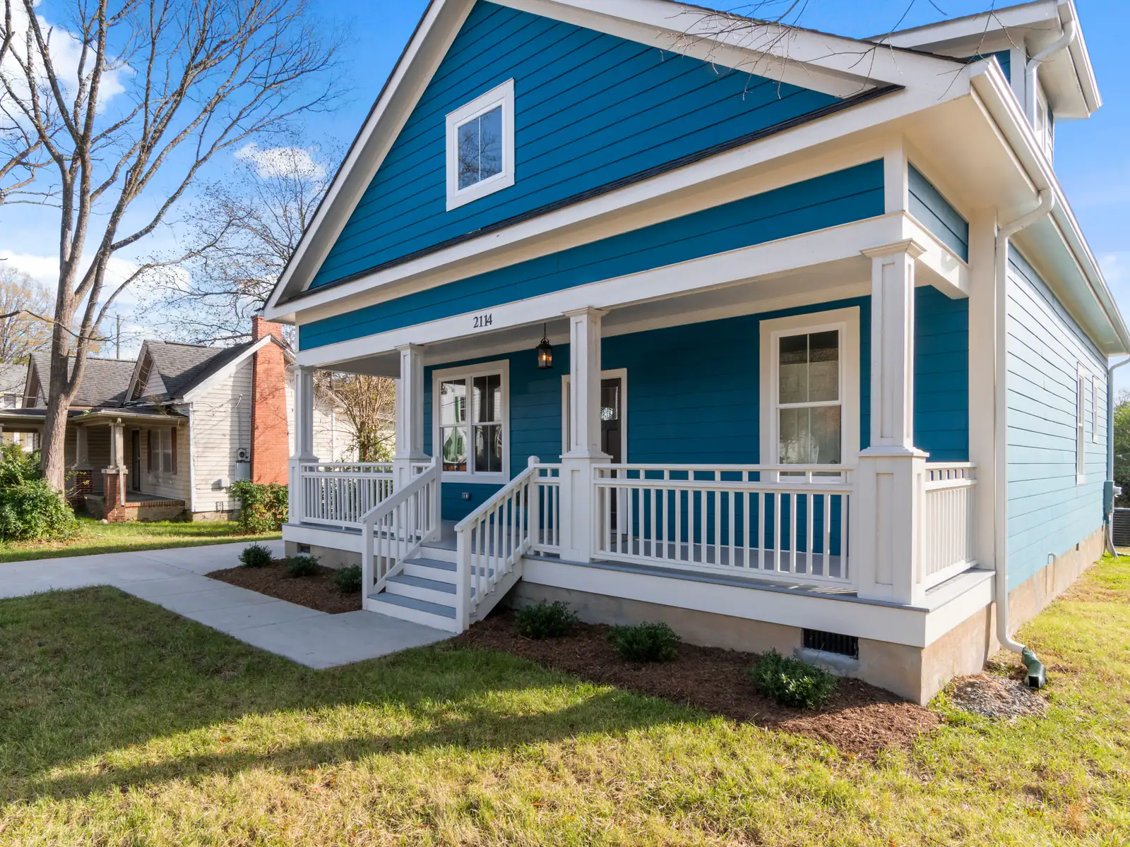 Blue bungalow with white porch railings and steps on a grassy corner lot