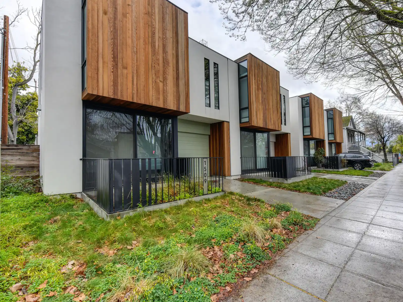 Modern townhomes with wood cladding beside a wide sidewalk and street trees