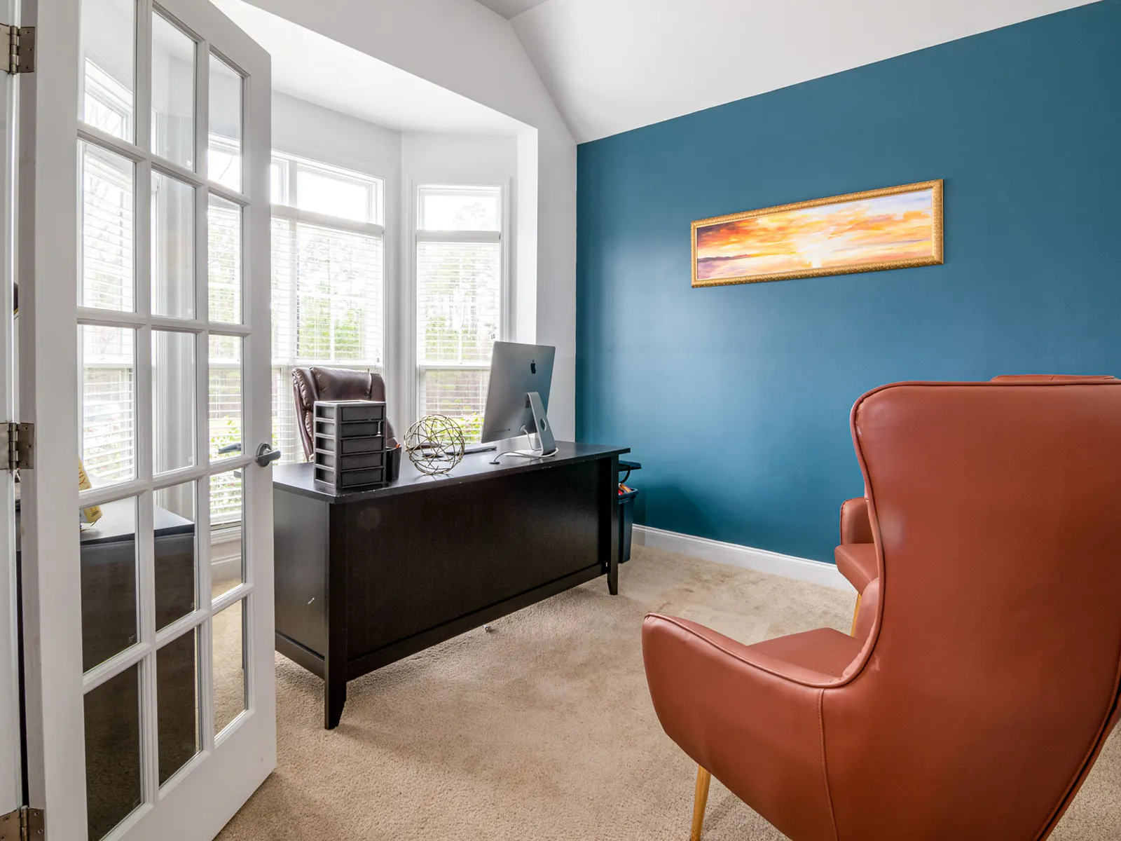 Office with a dark wooden desk, a blue wall and a leather armchair