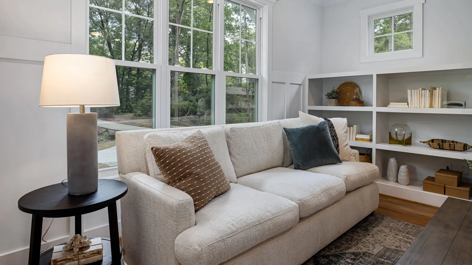 Bright living room with a cream sofa, table lamp and tall windows