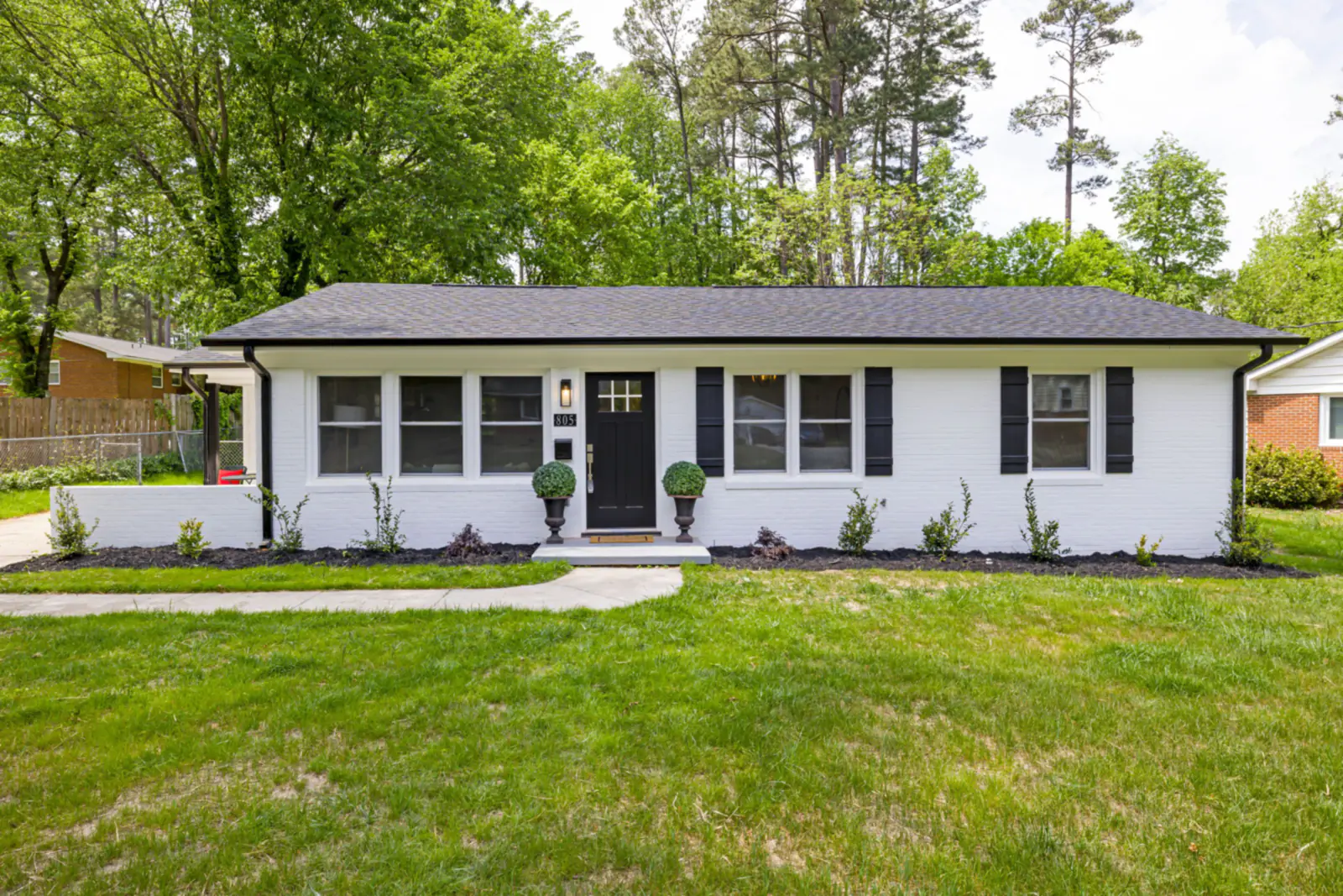 Single-storey white brick ranch house with black shutters and front lawn