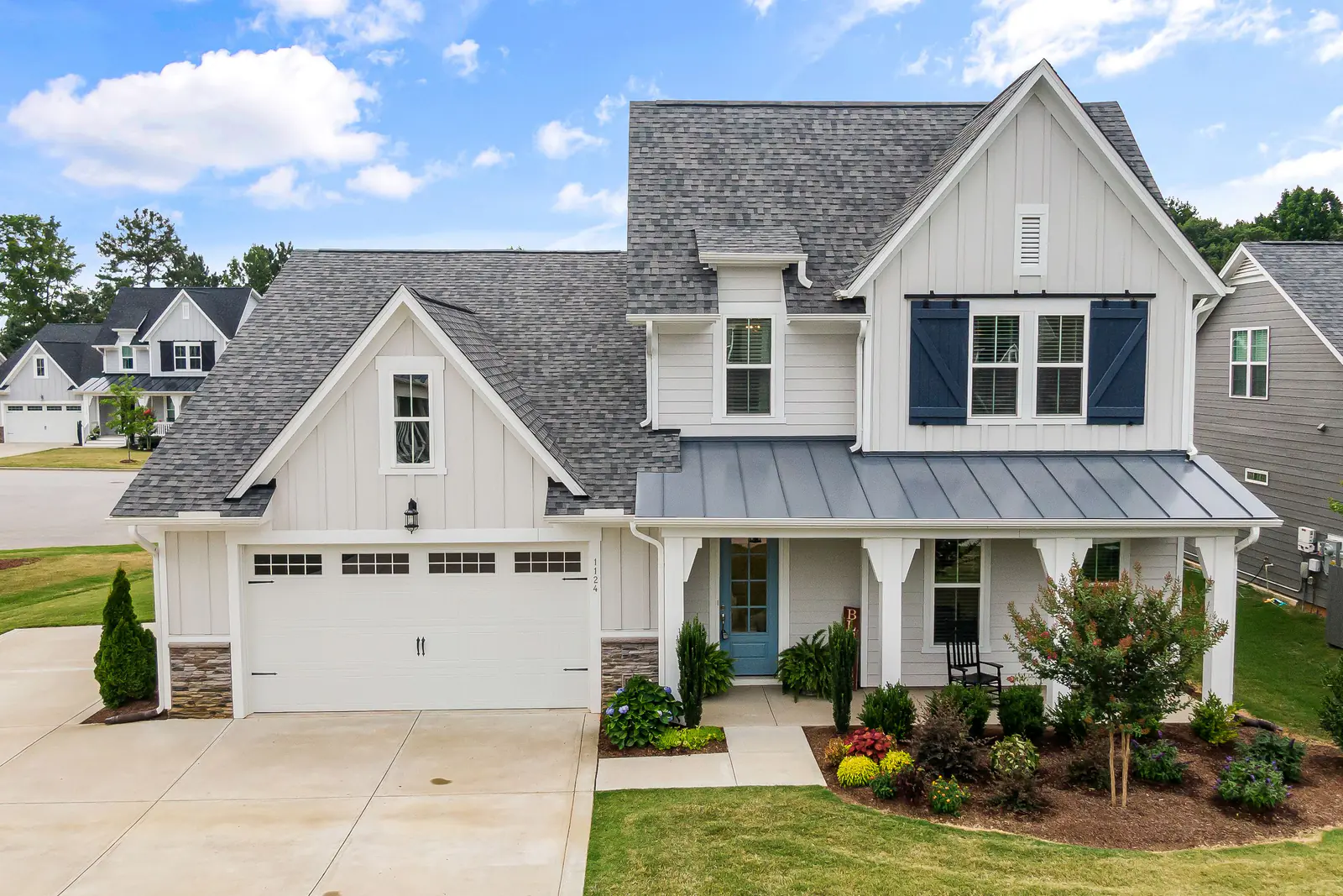 White board-and-batten modern farmhouse with metal porch roof and garage
