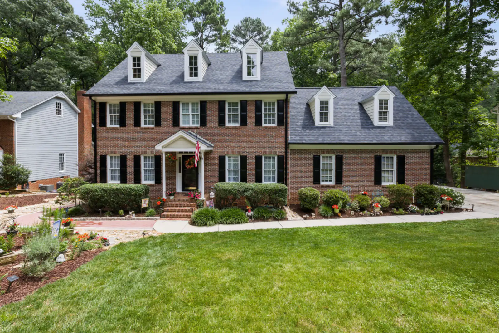 Two-storey brick colonial house with dormer windows and landscaped front lawn