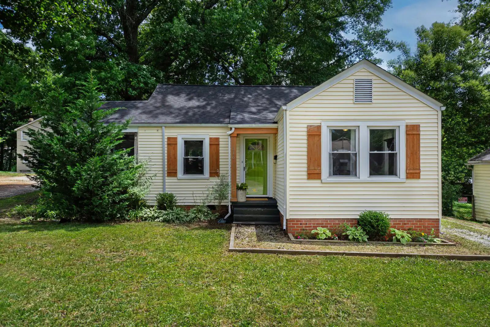 Small cream cottage with wooden shutters and a green front door