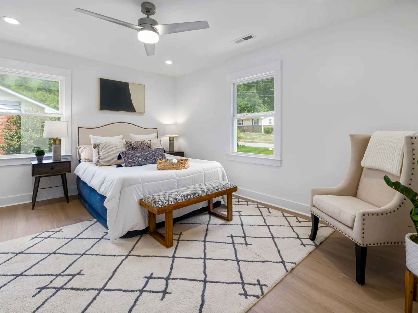Bright bedroom with a made bed, bench, armchair and patterned rug