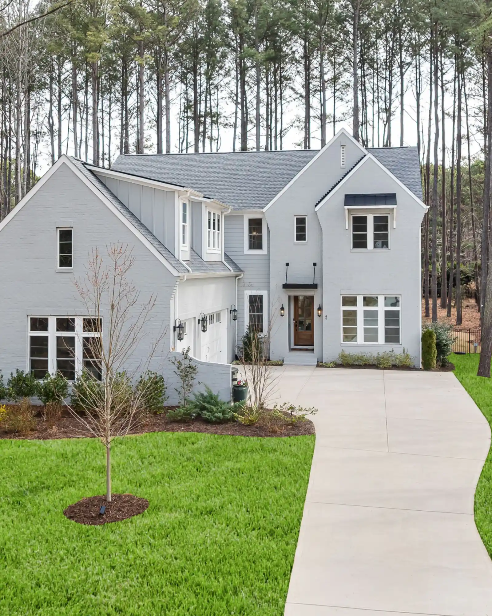 White brick house with a curved front walk among tall pine trees