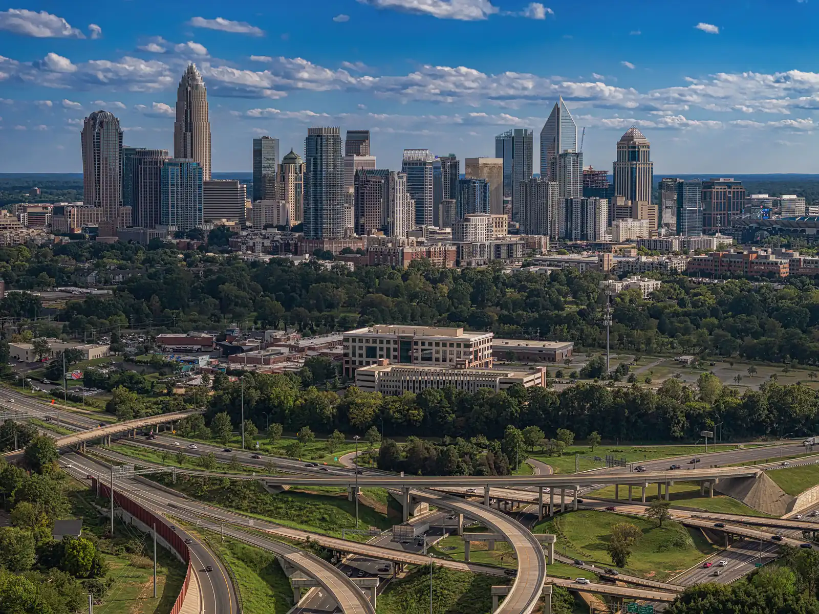 Charlotte skyline above green trees and highway interchanges on a clear day