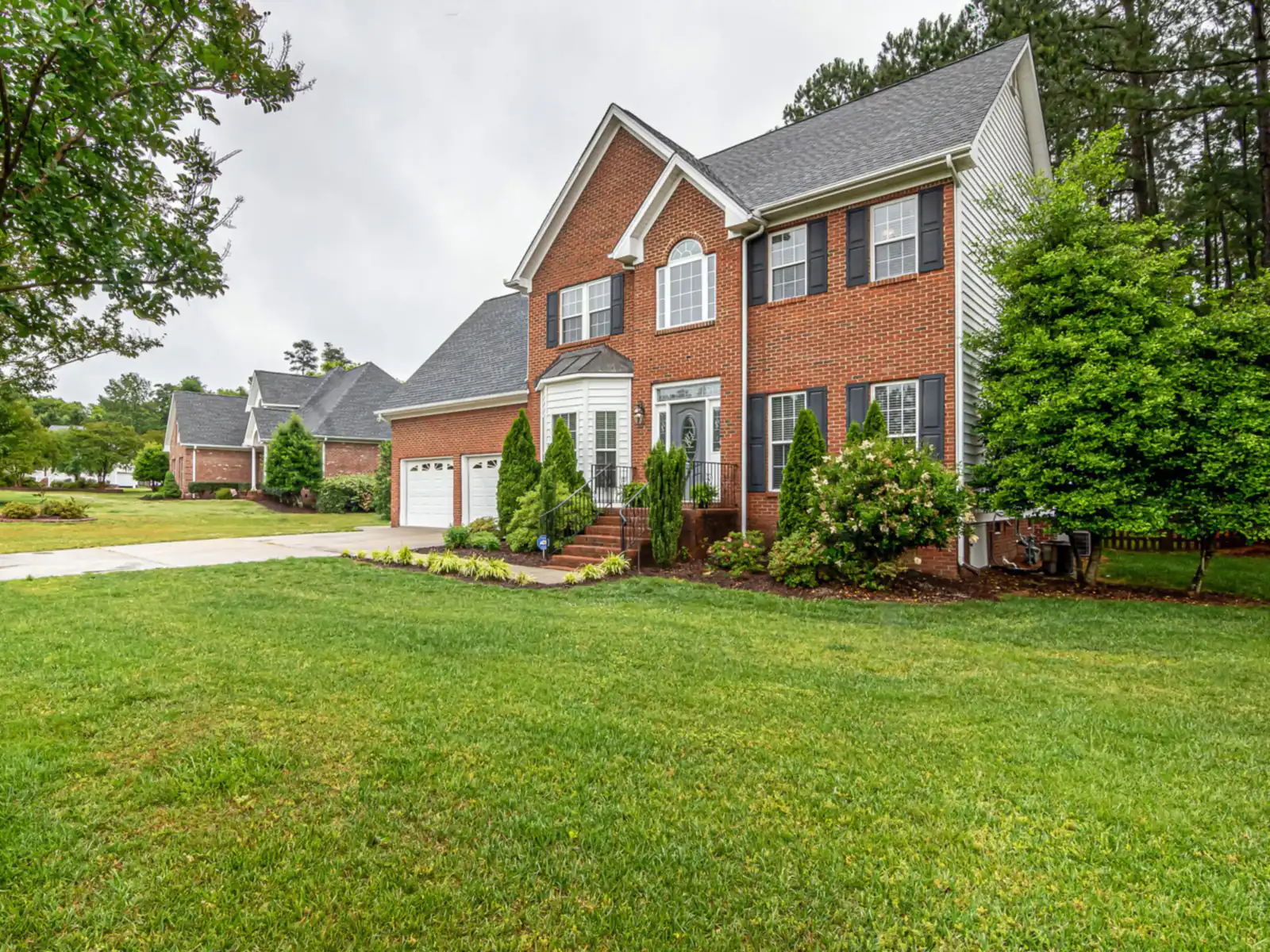 Two-storey brick house with dark shutters behind a broad green lawn
