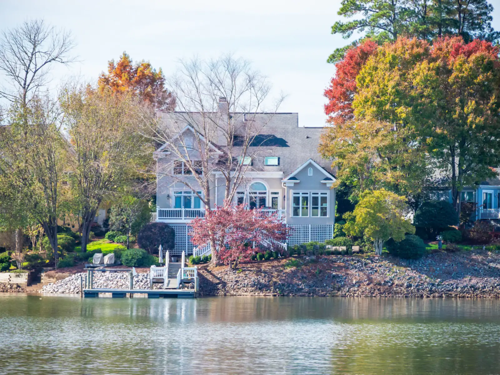 Lakefront house with a small dock, autumn trees and calm water